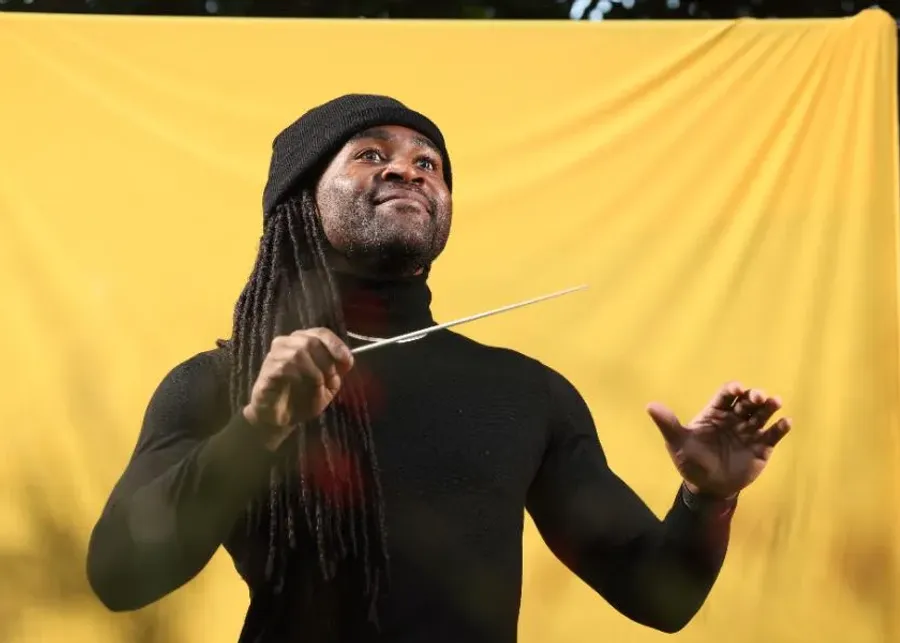 Alexander Blake conducting in front of a yellow backdrop.